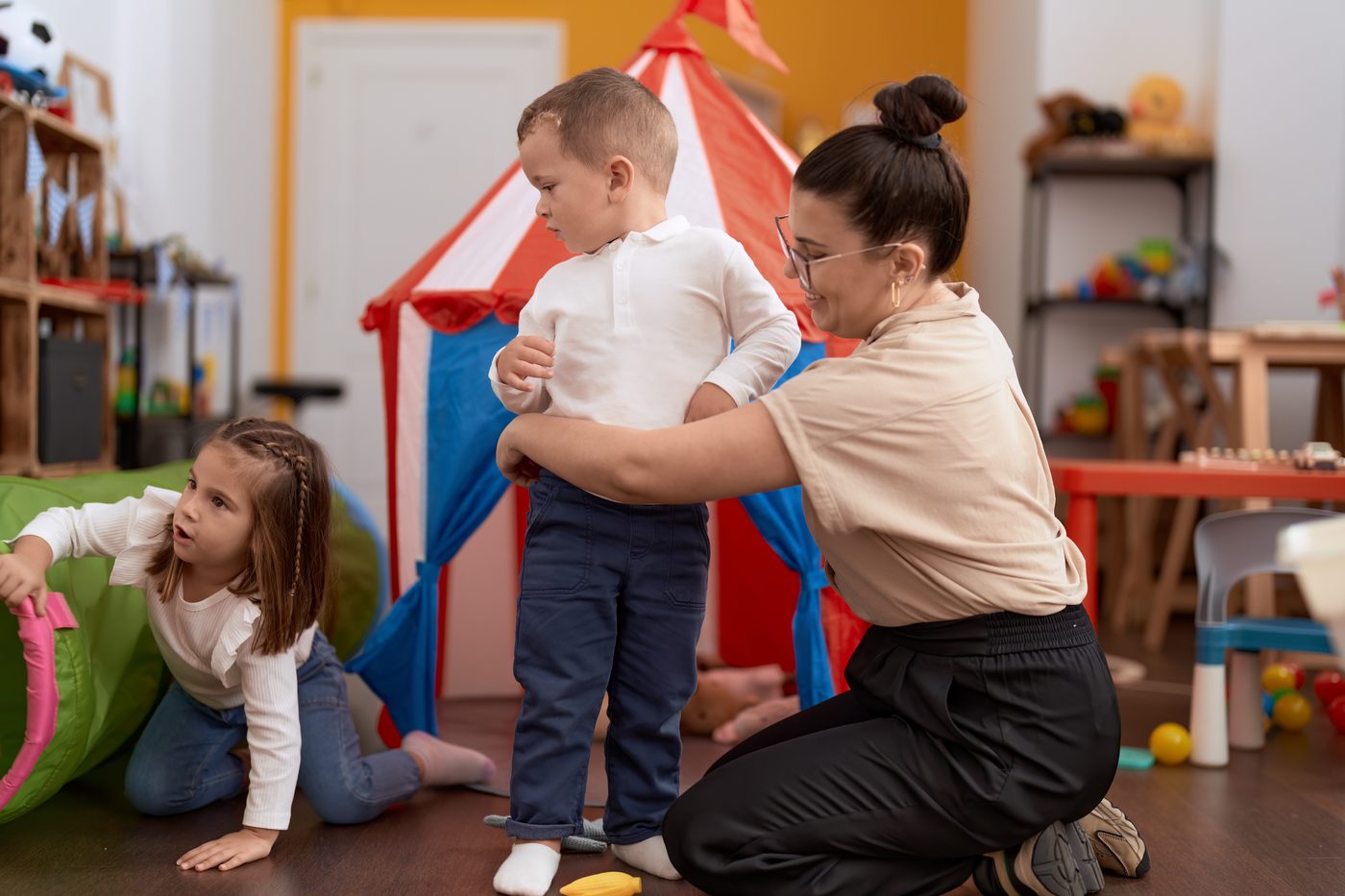 Educatoare care ține în brațe un băiețel la grădiniță, lângă alți copii