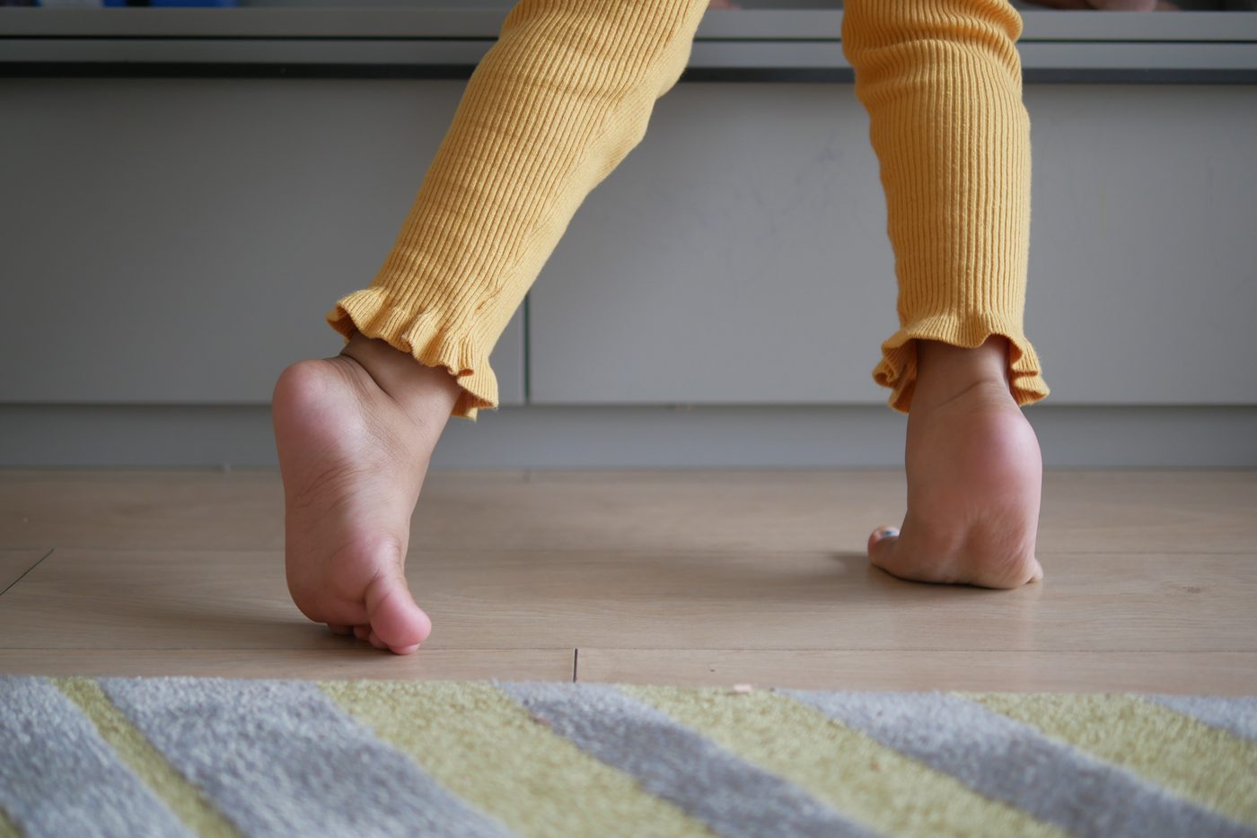 Copil care merge pe vârfuri, văzut de jos, pe podea