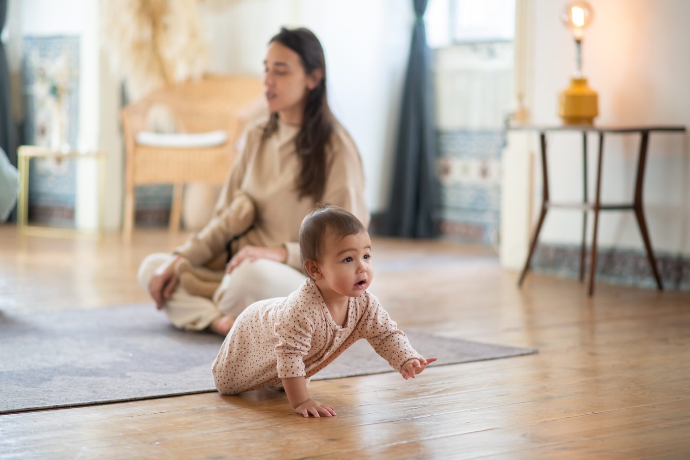 Bebeluș care se târăște pe saltea, cu mama în spate