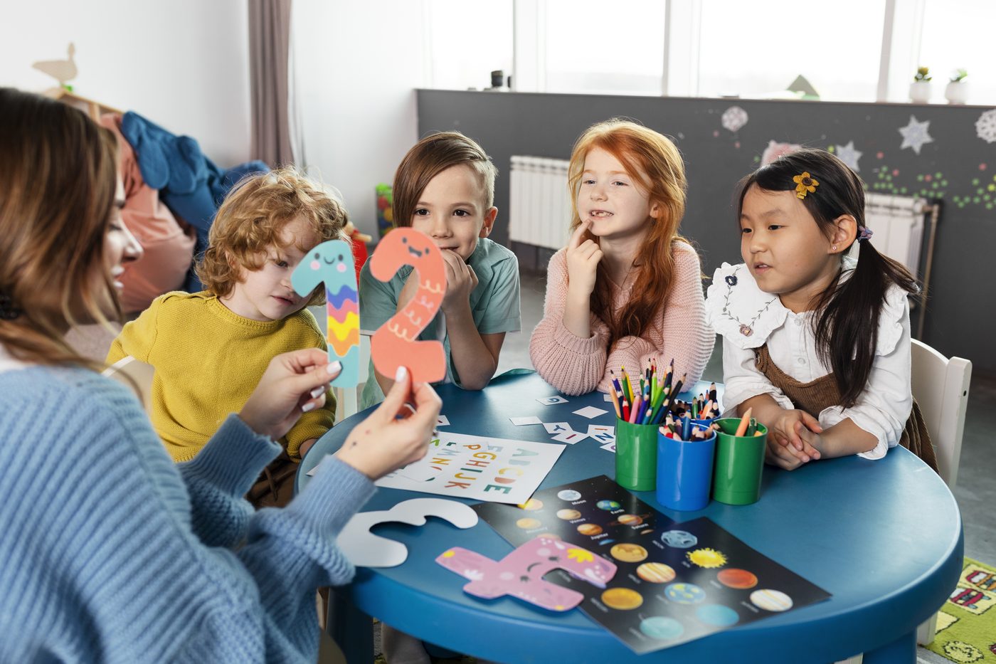 Copii de grădiniță la o masă de activități, împreună cu o educatoare