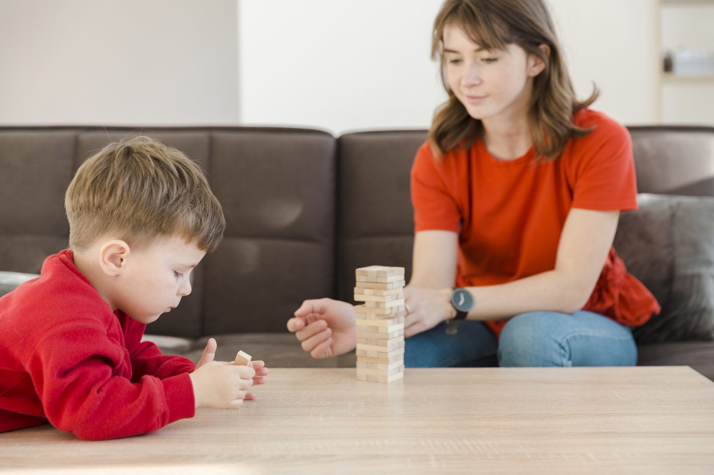 Băiat care construiește un turn de piese, lângă un adult