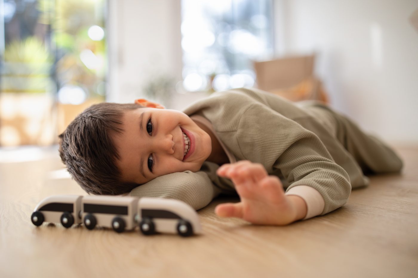 Băiețel întins pe podea, la nivelul ochilor cu un tren de lemn