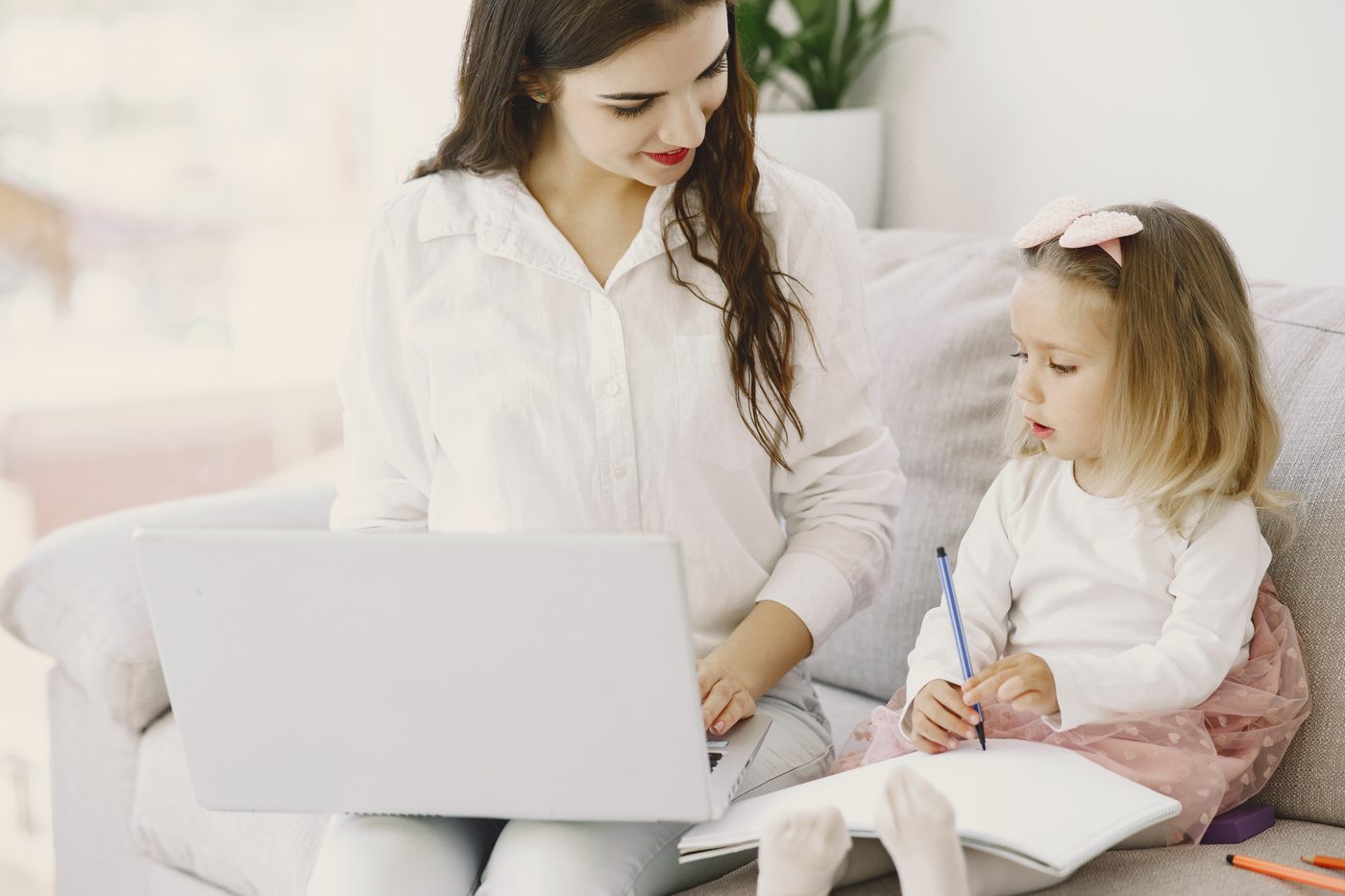 Părinte cu laptopul, lângă un copil care desenează